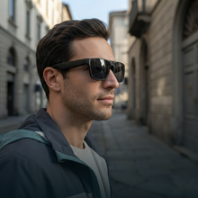 A man in a city street wearing black rectangular sunglasses and a dark gray hooded jacket, shown in a side profile view.